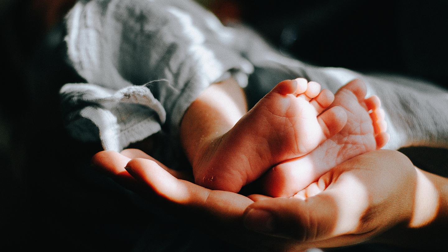 Bild på en vuxen hand som håller i ett par babyfötter